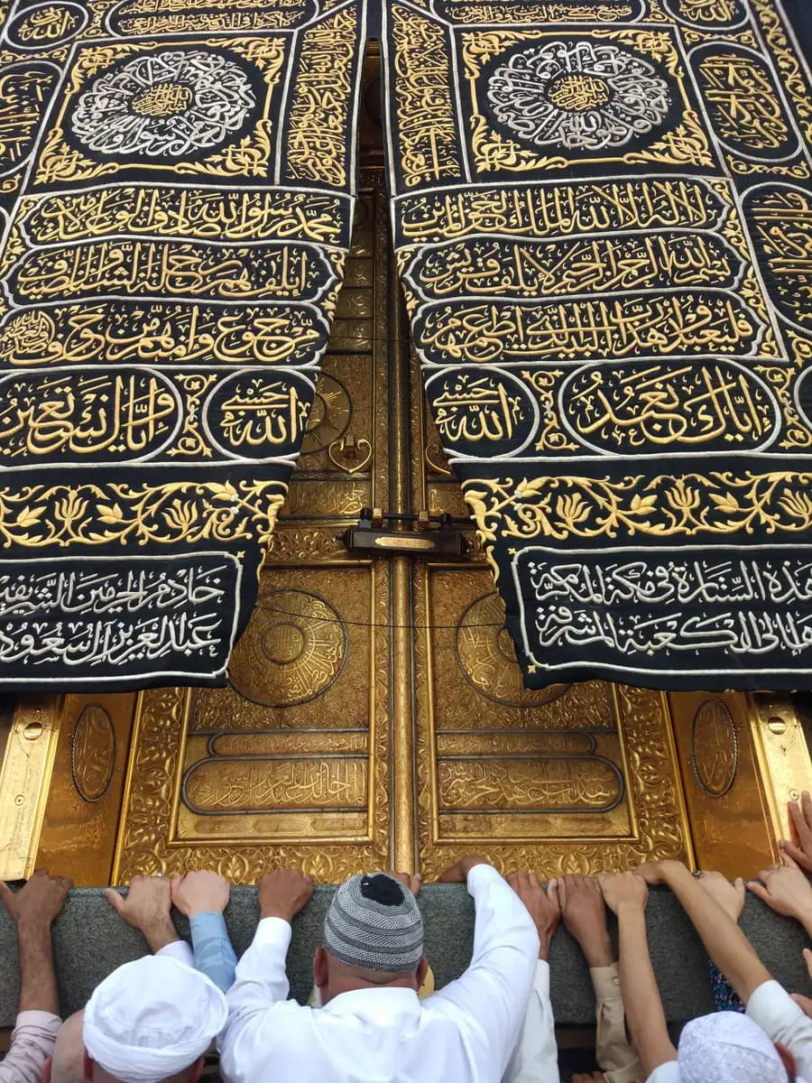 Close detail of the Kaaba's Kiswah door covering with gold embroidered calligraphy, pilgrims' hands reaching toward it
